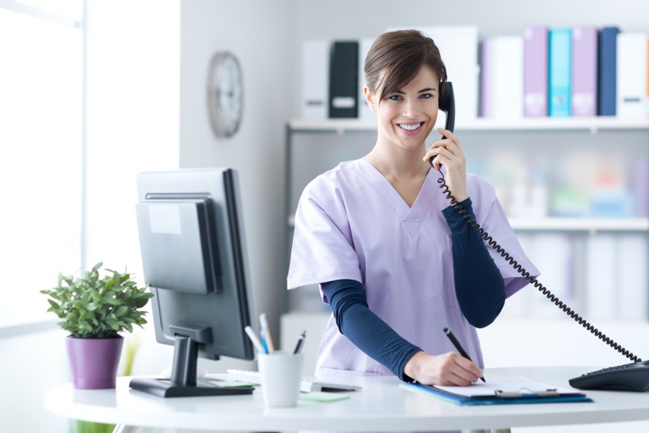 Medical billing and coding specialist in scrubs answers phone in a medical office.