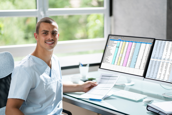 Medical billing and coding professional sits at computer displaying spreadsheets.